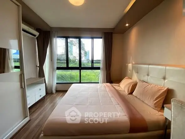 Spacious bedroom with large window and modern furnishings, offering a serene view and ample natural light.