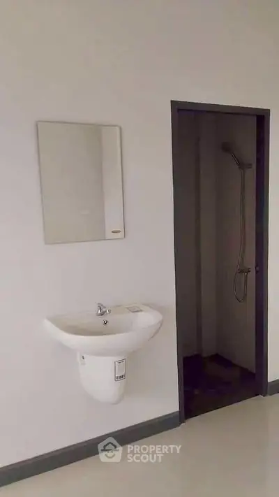 Minimalist bathroom with wall-mounted sink and shower area in modern apartment.