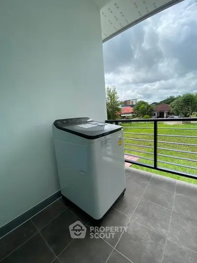 Spacious balcony with washing machine and scenic view of lush greenery.