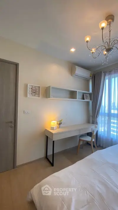 Elegant bedroom with modern decor, featuring a stylish desk, chandelier, and large window for natural light.