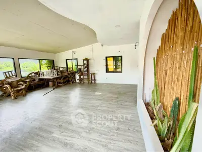 Spacious living room with large windows and modern flooring, featuring rustic wooden furniture and decorative cacti.