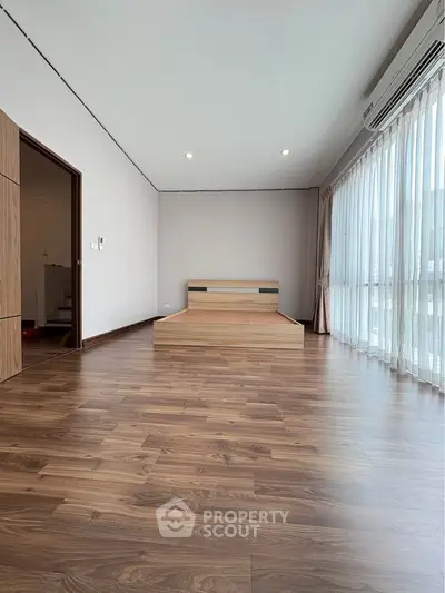 Spacious bedroom with wooden flooring and large windows for natural light.