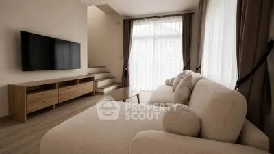 Modern living room with cozy beige sofa and wall-mounted TV, featuring natural light from large windows.