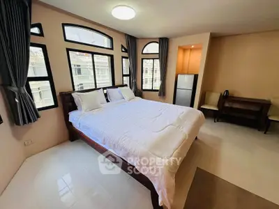 Spacious bedroom with large windows and modern furnishings in a city apartment.