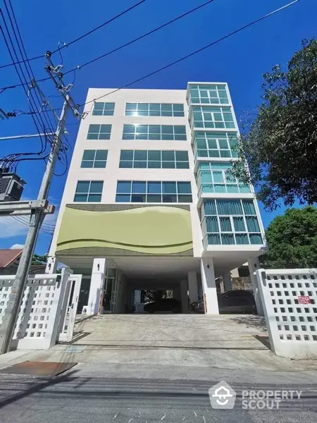 Modern multi-story building with ample parking and striking facade, nestled in a vibrant neighborhood under a clear blue sky.