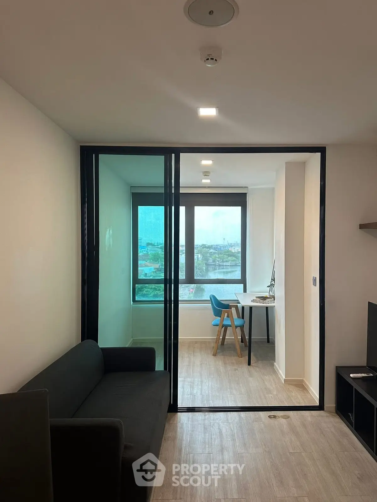 Modern living room with glass partition and city view, featuring sleek furniture and natural light.