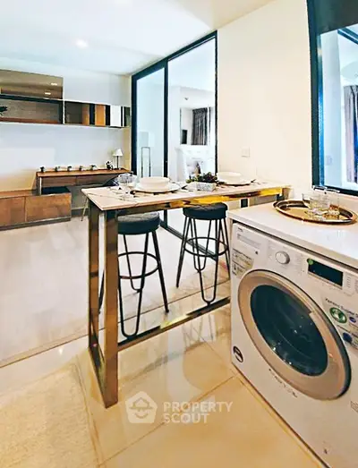 Modern open-plan kitchen with dining area and washing machine, featuring sleek design and contemporary furnishings.
