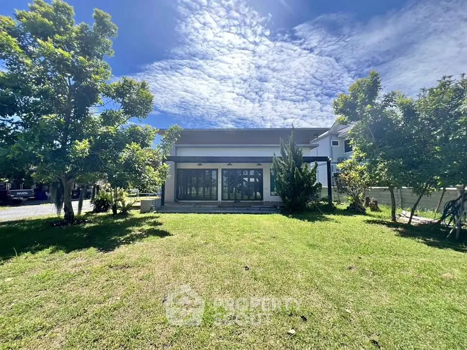 Modern house with large windows and lush green lawn under a clear blue sky.