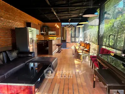 Spacious open-layout living area with modern kitchen and stylish seating, featuring exposed brick walls and wooden flooring.