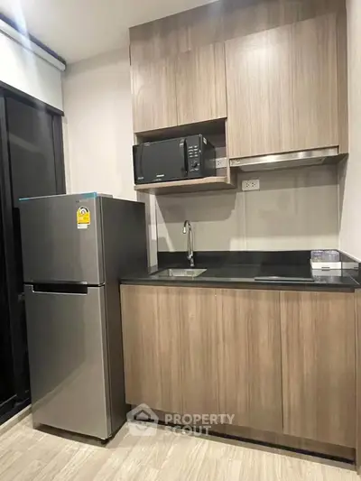 Modern kitchen with sleek cabinetry, stainless steel fridge, and microwave in a compact layout.