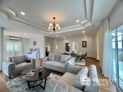 Spacious modern living room with elegant gray sofas, stylish lighting, and open layout leading to dining area.