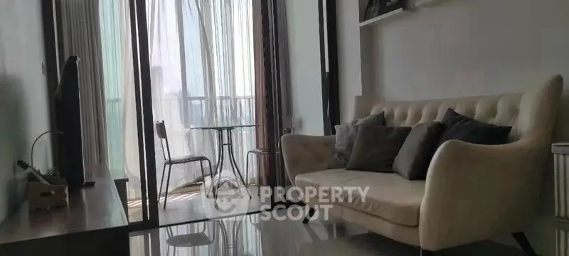 Modern living room with elegant sofa and glass table leading to a bright balcony view.