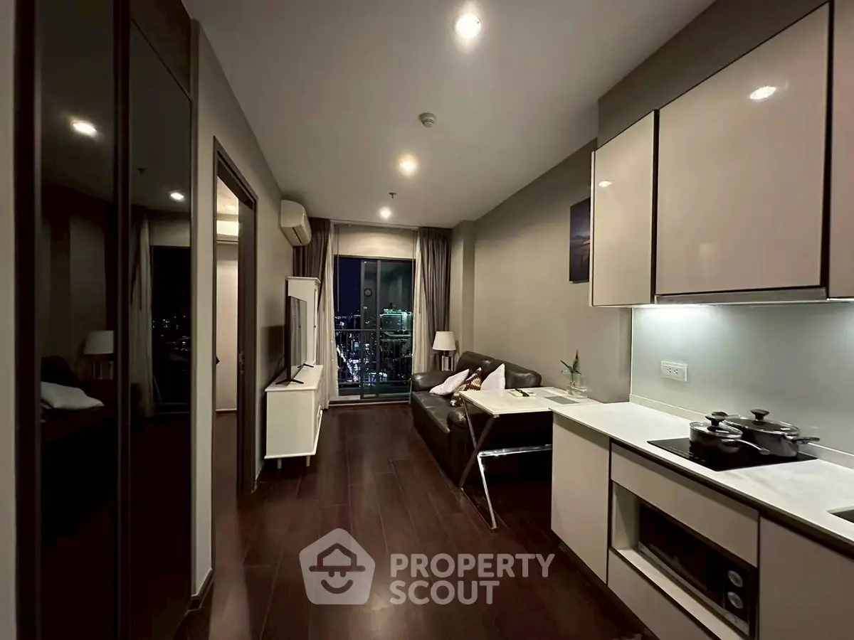 Modern apartment interior with sleek kitchen and cozy living area, featuring city view from large window.