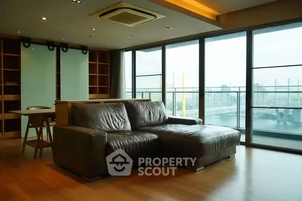 Spacious living room with leather sofa and stunning city view from large windows.
