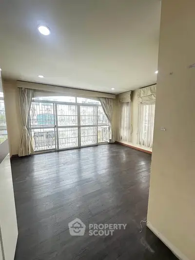 Spacious living room with large windows and dark wood flooring in a modern apartment.