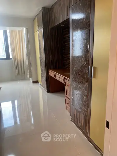 Spacious bedroom with built-in wooden wardrobe and large window for natural light.