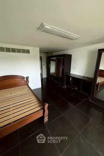 Spacious bedroom with dark tile flooring and wooden furniture, ideal for modern living.