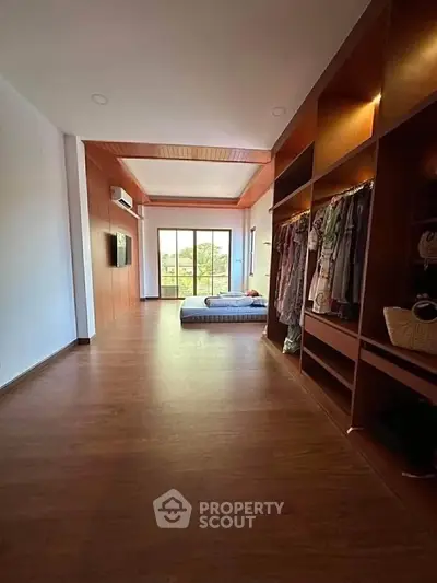 Spacious bedroom with wooden flooring and large windows offering natural light and garden view.