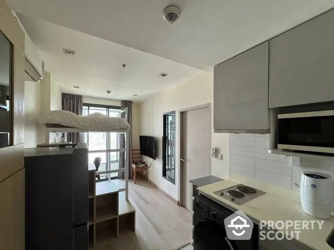 Modern studio apartment with integrated living space, featuring a sleek kitchen with built-in appliances, a cozy sleeping area, and ample natural light from the balcony doors.