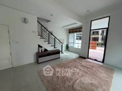 Spacious modern living room with large window and staircase, ideal for family gatherings.