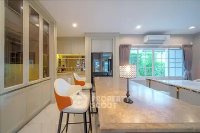 Luxurious kitchen with marble island and modern bar stools, featuring large windows and elegant cabinetry.