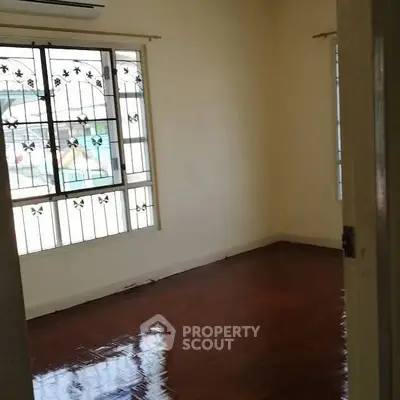 Spacious empty room with polished wooden floors and large window with decorative grill.