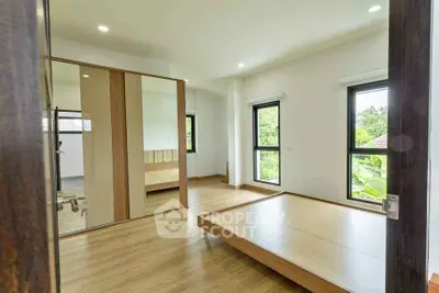 Spacious bedroom with large windows and wooden flooring, offering a serene view of greenery.