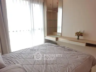 Cozy bedroom with soft lighting and modern furnishings, featuring a large window with sheer curtains.