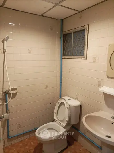 Compact bathroom with full tiling, shower area, toilet, and pedestal sink, featuring a small diamond-patterned window for natural light.