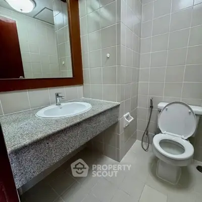 Modern bathroom with sleek fixtures and neutral tiles, featuring a spacious countertop and mirror.