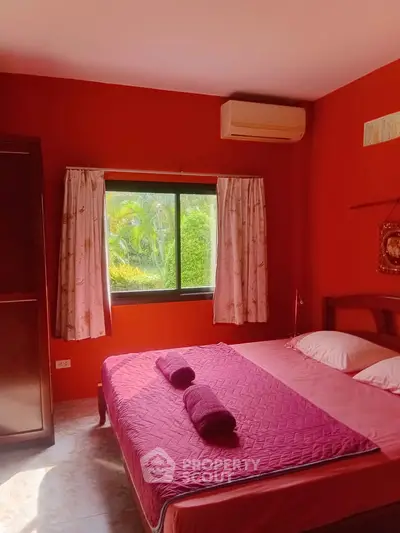Cozy bedroom with vibrant red walls and garden view, featuring a comfortable bed and air conditioning.