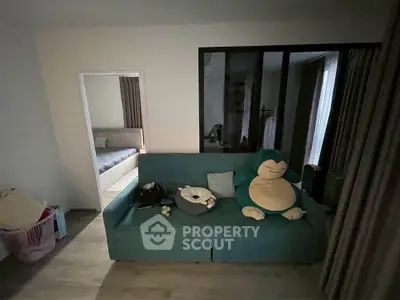 Cozy living room with teal sofa and plush toys, adjacent to a bedroom with soft lighting.