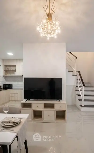 Modern living room with elegant chandelier and sleek staircase in a stylish home interior.