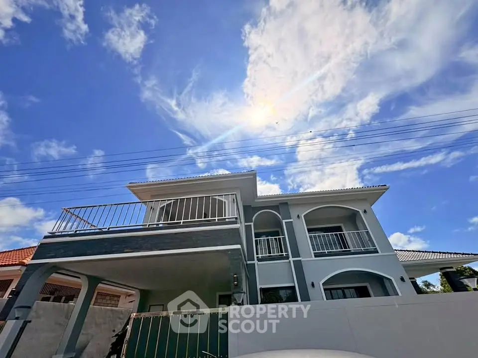 Stunning modern two-story house with spacious balcony and elegant facade under a bright blue sky.