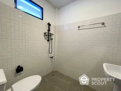 Pristine white-tiled bathroom featuring a modern shower system, sleek toilet, and a bidet, complemented by a spacious design and ample lighting.