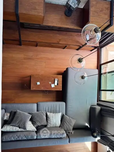 Modern living room with stylish gray sofa and wooden flooring, featuring large windows and contemporary lighting.