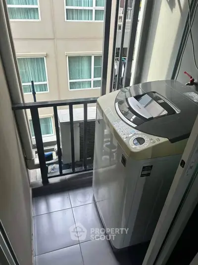 Compact balcony with washing machine in modern apartment building.