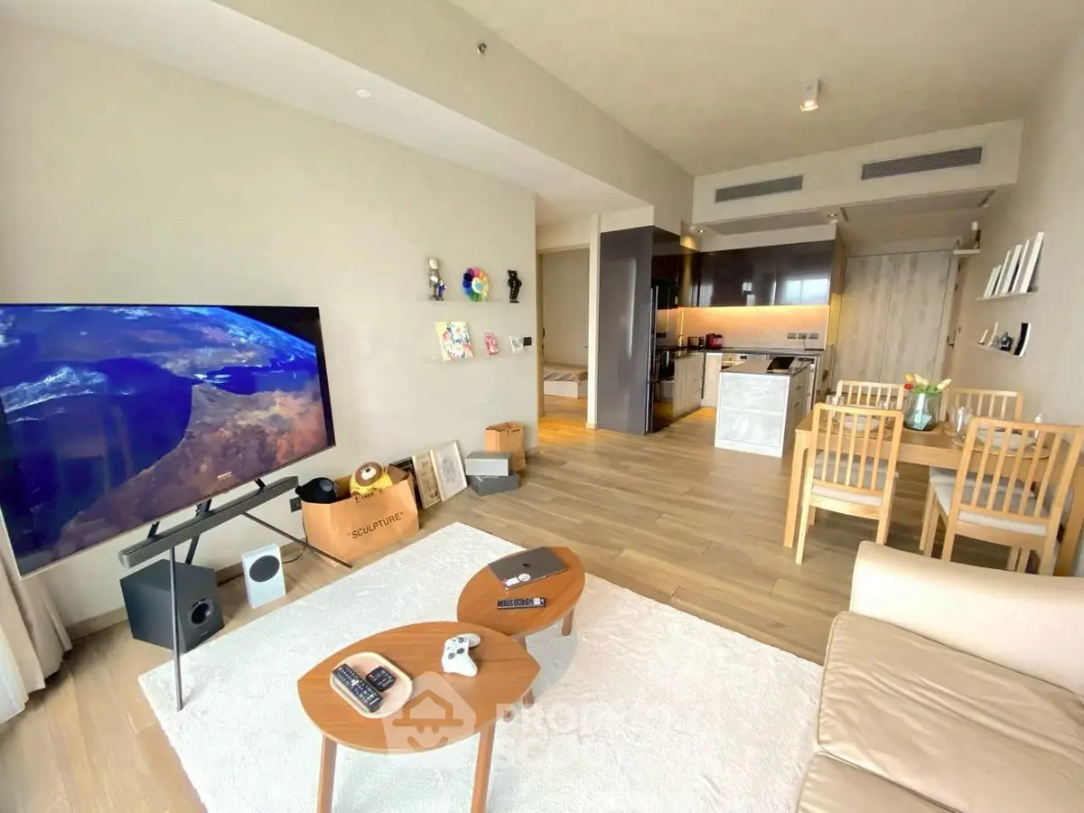 Modern living room with open kitchen, featuring stylish furniture and large TV, perfect for entertaining.