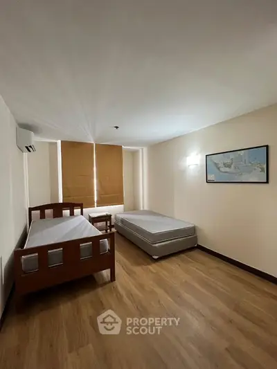 Spacious bedroom with two single beds and wooden flooring, perfect for comfortable living.