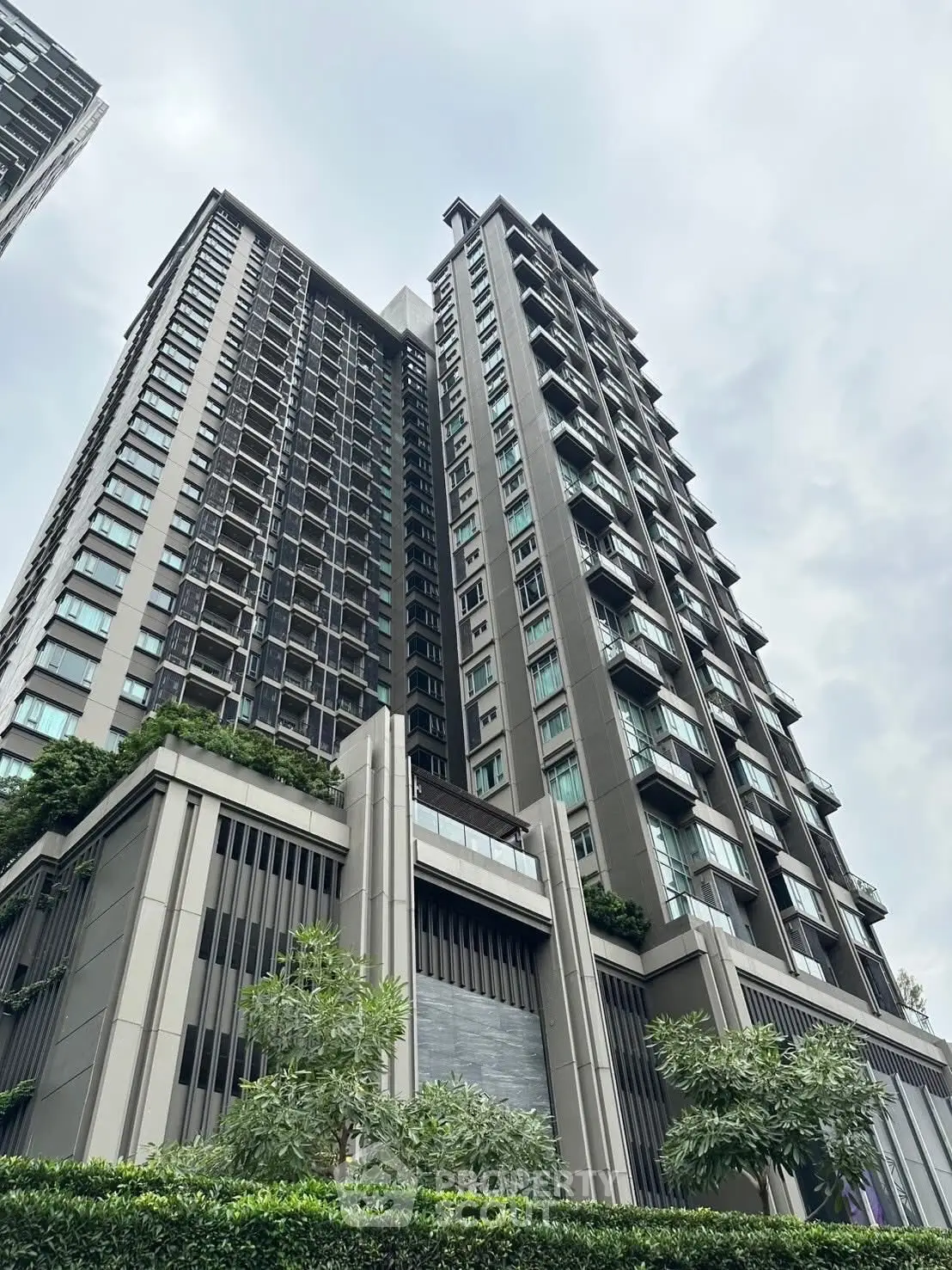 Modern high-rise building with sleek design and lush greenery in urban setting.