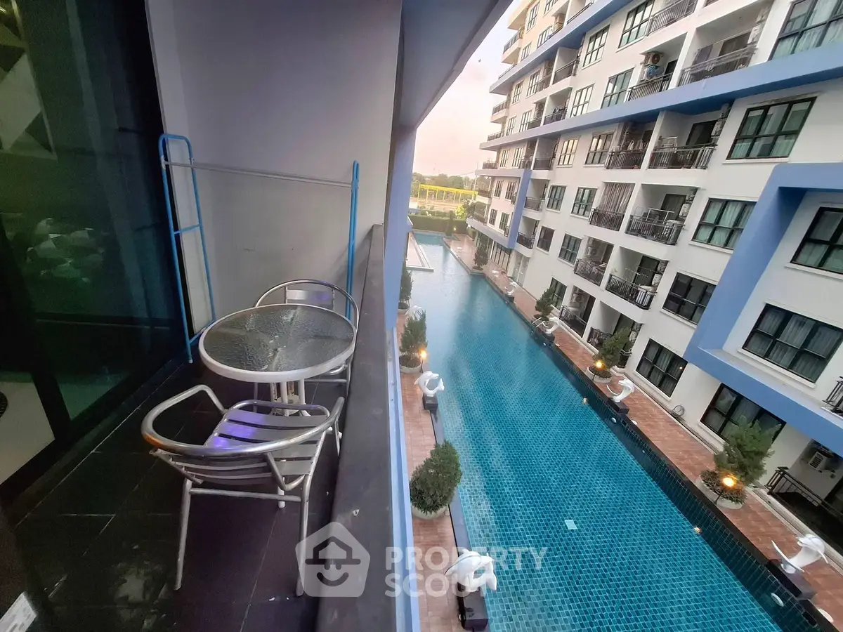Modern apartment balcony overlooking a luxurious pool with stylish outdoor seating.