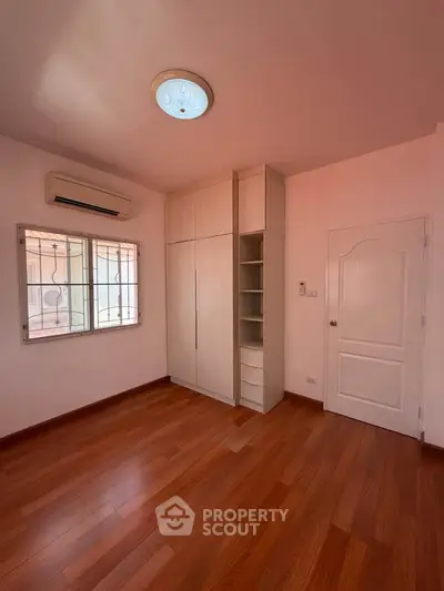Spacious bedroom with wooden flooring and built-in wardrobe, featuring air conditioning and natural light.