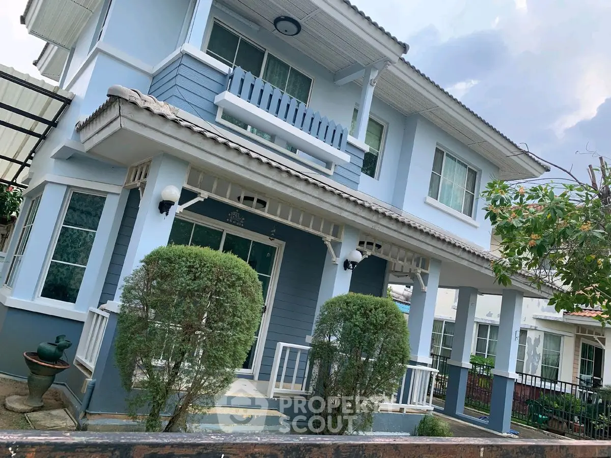 Charming two-story blue house with lush greenery and inviting porch.