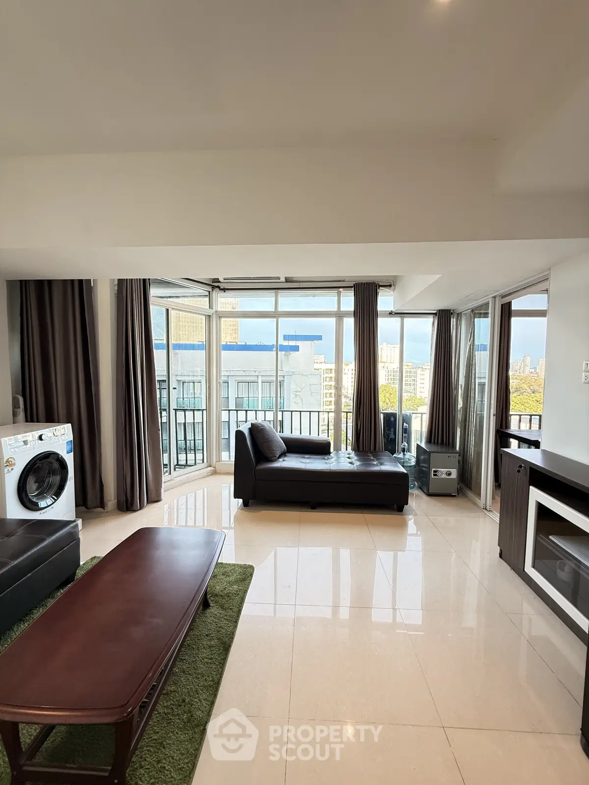 Spacious living room with modern furniture and city view, featuring a washing machine and large windows.