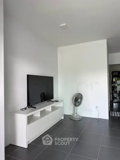 Modern living room with sleek TV stand and fan, featuring minimalist design and tiled flooring.