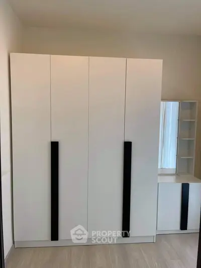 Modern white wardrobe with sleek black handles in a minimalist bedroom setting.