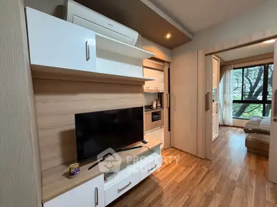 Modern living room with wooden flooring and stylish TV unit, leading to a cozy bedroom with large windows.
