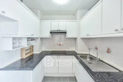 Modern kitchen with sleek white cabinets and black countertops, featuring a built-in stove and stainless steel sink.