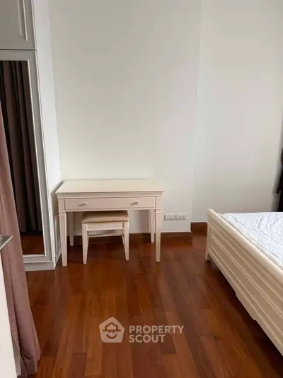 Elegant bedroom with wooden flooring and classic white furniture, featuring a bed and a stylish vanity desk.