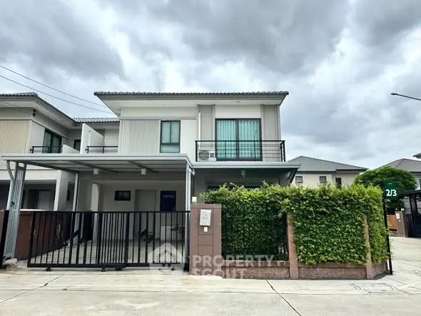 Modern two-story house with gated driveway and lush greenery under cloudy skies.